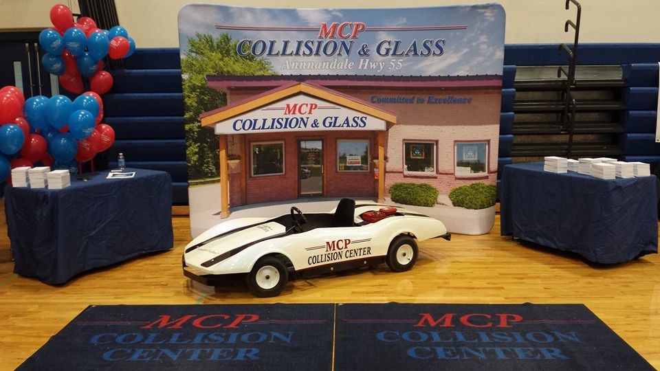 MCP Collision & Glass trade-show booth with the storefront banner, a custom show go-kart, and red and blue balloons