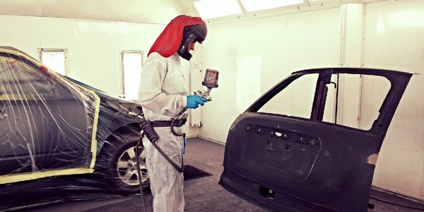 MCP painter in a red spray hood painting a vehicle panel in the downdraft booth